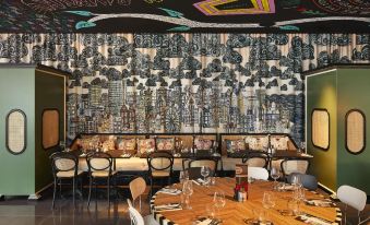 a dining room with a round table surrounded by chairs and a mural on the wall at Mama Shelter Lille