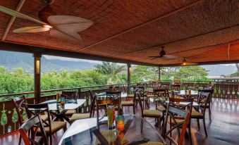 a restaurant with wooden tables and chairs , a thatched roof , and a view of the mountains at Paradise Bay Resort