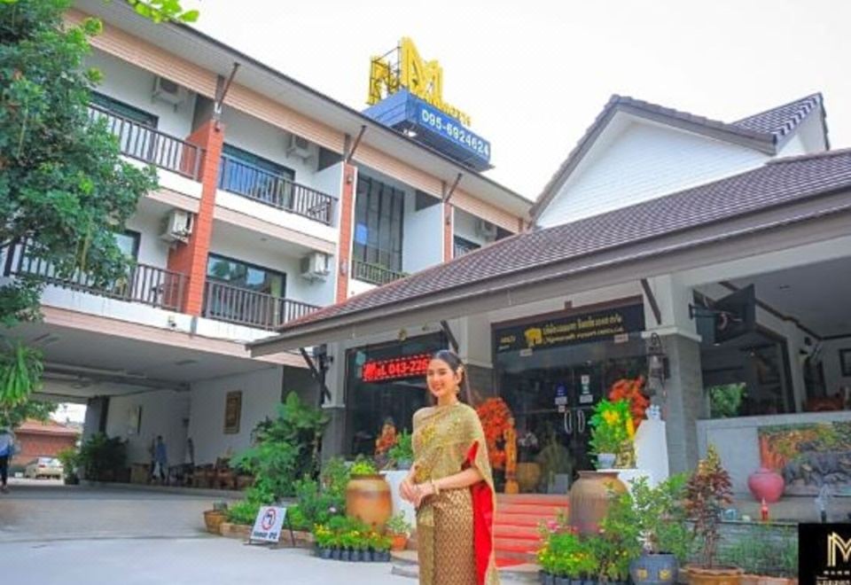 "a woman in a traditional thai dress stands in front of a large building with a sign that reads "" thanon "" on it" at Mammoth Resort