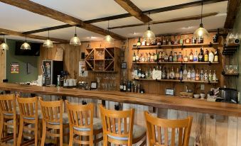 a wooden bar with several chairs and stools , as well as a variety of bottles and cups on the counter at The Birchwood Inn