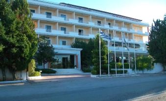 a large white building with many windows , surrounded by trees and flags , on a city street at Hotel Philippos