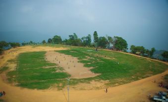 a large grassy field with a dirt path leading to a volleyball net , surrounded by trees at Hotel Srinagar