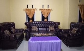 a living room with a black leather couch , two chairs , and a purple table in the center at Sinar Harapan