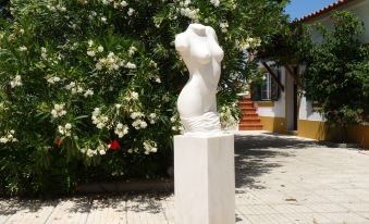 a white statue of a woman on a pedestal in front of a building with green bushes and flowers at MirArte