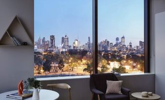 a modern living room with a large window that overlooks a cityscape at night , and two chairs placed in front of the window at The Larwill Studio Melbourne - Art Series