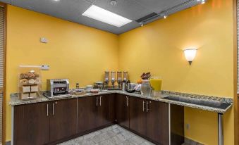 a kitchen area with yellow walls , brown cabinets , and various appliances such as a toaster and a microwave at Quality Inn & Suites Bay Front