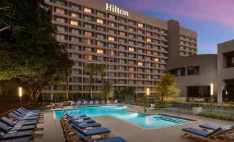 a large hotel with a swimming pool and lounge chairs in front of it at night at Hilton Los Angeles-Culver City, CA