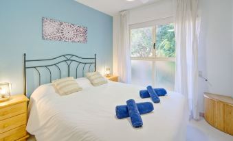 a bed with white sheets and a blue comforter , along with two pillows and a window in the background at Zeus