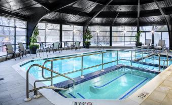 an indoor swimming pool surrounded by glass walls , with a diving board and chairs nearby at Desmond Hotel Malvern, a DoubleTree by Hilton