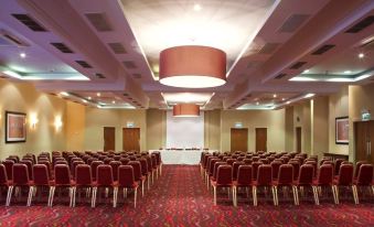 a large conference room with red carpet and chairs , a white screen , and a red carpet on the floor at Riverside Lodge Hotel