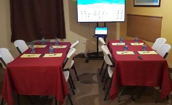 a conference room with multiple tables and chairs , a large screen on the wall , and windows at Amelia Extended Stay & Hotel