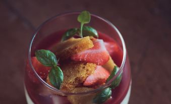 a glass of red fruit - infused drink with a basil leaf on top , placed on a wooden table at The New Inn - Yealand