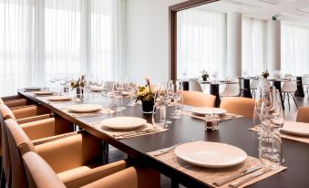 a large dining room with multiple tables set for a formal event , featuring white plates and wine glasses at AC Hotel Paris le Bourget Airport