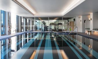 an indoor swimming pool with blue and black tiles , surrounded by glass walls , and equipped with exercise equipment at Ovolo Woolloomooloo