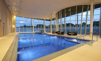 an indoor swimming pool surrounded by glass walls , with lounge chairs placed around the pool area at Hilton at St.George's Park, Burton Upon Trent
