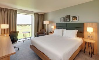 a large bed with white sheets is in a room with a chair and desk at Hilton Garden Inn Doncaster Racecourse