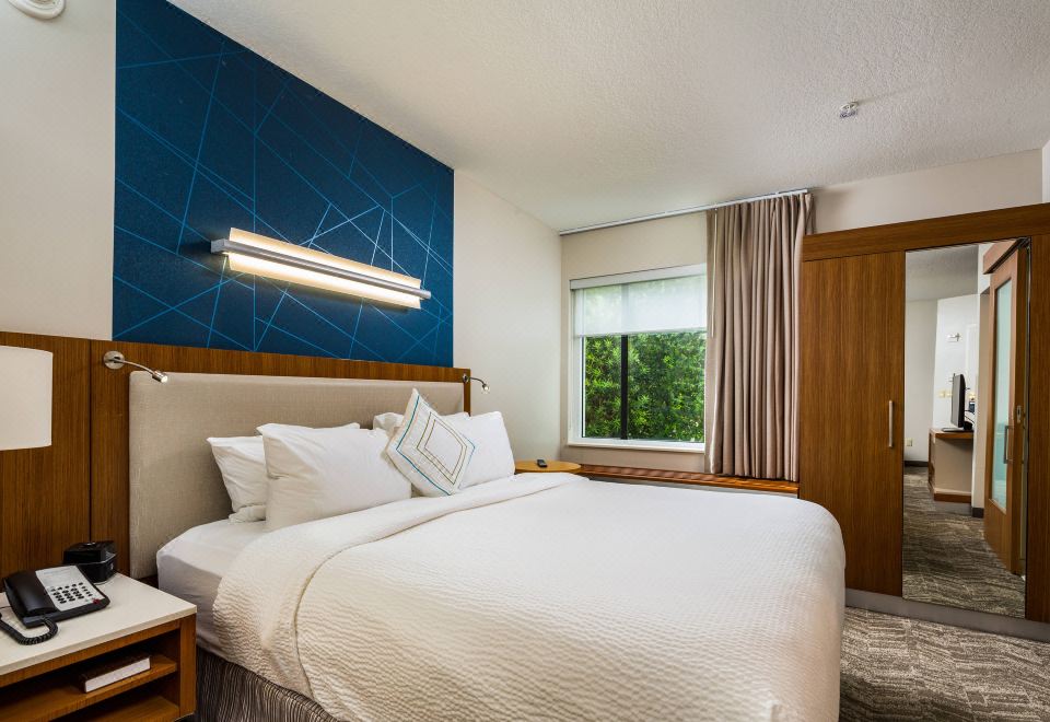 a large bed with white linens is in a room with a blue accent wall and wooden headboard at SpringHill Suites Vero Beach