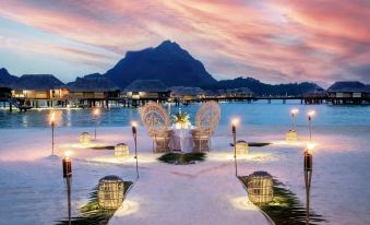 a romantic dinner setup on a beach , with white chairs and candles set up on the sand at Le Bora Bora by Pearl Resorts