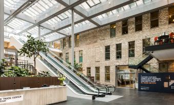 a modern office building with an open atrium , featuring a large glass ceiling and an escalator at NH Den Haag