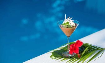 a glass of chocolate dessert is placed on a table next to a pool , with a flower and palm leaf nearby at Navutu Stars Resort