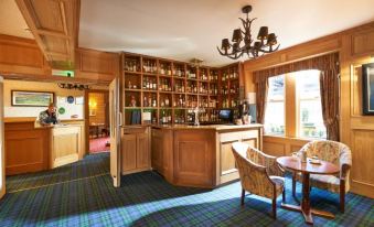 a bar area with wooden walls , shelves filled with bottles , and a chandelier hanging from the ceiling at Loch Kinord Hotel