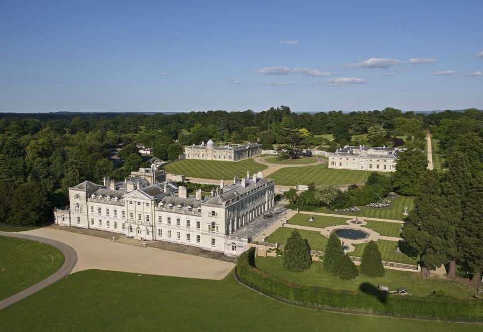 aerial view of a large white building surrounded by green grass and trees , with a fountain in the foreground at The Woburn