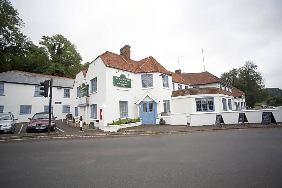 a white building with red tile roofs and green signs , located on a street corner at Shillingford Bridge Hotel