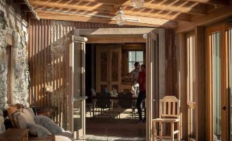 a man and a woman are standing in a room , looking out the window at a wooden house at The Headwaters Eco Lodge