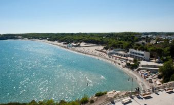 a beautiful beach with clear blue water , surrounded by lush green trees and a crowd of people enjoying the sunny day at Hotel Belvedere