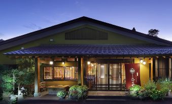 a traditional japanese house with a green roof and red door , surrounded by potted plants and lit up at night at Shikimitei Fujiya