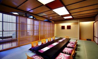 a dining room with a long wooden table surrounded by chairs , and a television mounted on the wall at Biwako Ryokusuitei