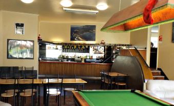 a bar with a pool table in the center , surrounded by chairs and tables , as well as a dining table at Lufra Hotel and Apartments