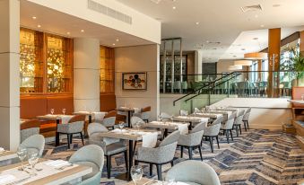 a modern dining room with several tables and chairs , as well as a staircase in the background at Crowne Plaza Reading East