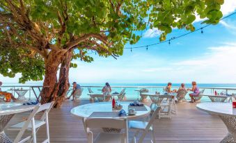 a group of people sitting at tables on a wooden deck overlooking the ocean , enjoying their time together at Travellers Beach Resort
