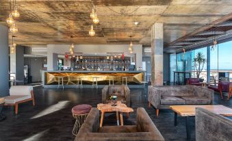 a modern bar with wooden stools and tables , a gold bar , and a couch in the foreground at AP Maria Nova Lounge