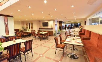 a large , empty restaurant with multiple dining tables and chairs , as well as a tv on the wall at Asian Hotel