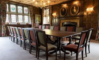 a large dining room with a wooden table surrounded by chairs , all facing the other side at Ockenden Manor Hotel & Spa