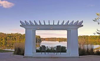 a white gazebo with a pergola and chairs is located near a lake , offering a serene view of the water at Lakeside Hotel Casino