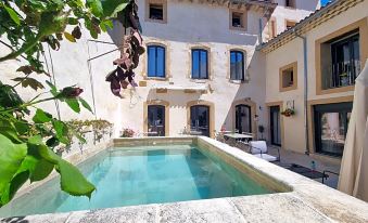 a large swimming pool is surrounded by a white building with red accents and green plants at La Bastide