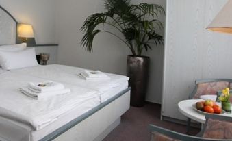 a clean and tidy hotel room with a white bed , towels , and a potted plant at Falkensee