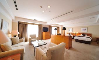 a large , well - lit hotel room with a couch , chairs , tables , and a desk in the corner at Hiroshima Airport Hotel