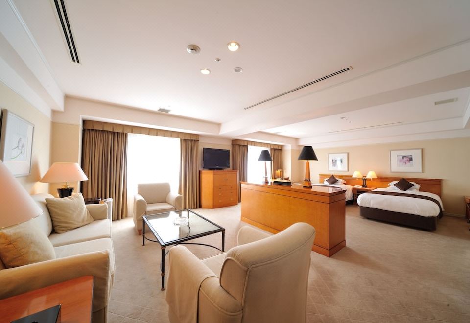 a large , well - lit hotel room with a couch , chairs , tables , and a desk in the corner at Hiroshima Airport Hotel