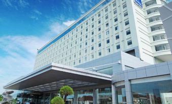 a large white hotel with a blue roof and a sign in front of it at Novotel Bangka - Hotel & Convention Centre