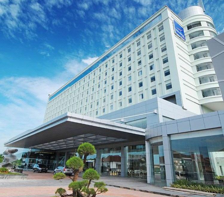 a large white hotel with a blue roof and a sign in front of it at Novotel Bangka - Hotel & Convention Centre