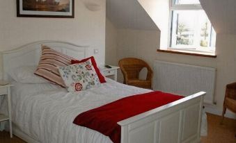 a white bed with red blankets and pillows is in a room with a window at The Foxham