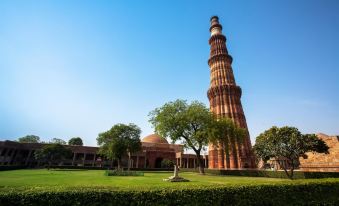 a red brick tower with a tall spire in the background , surrounded by a grassy area and trees at La Residence