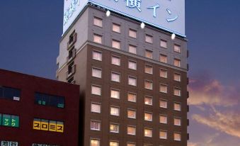 a tall building with a large white sign on the side , illuminated at night against a cloudy sky at Toyoko Inn Shizuoka Fujieda Eki Kita Guchi