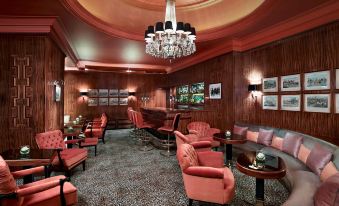 a luxurious bar with red velvet chairs , a crystal chandelier , and framed pictures on the walls at Hotel Bristol, a Luxury Collection Hotel, Vienna
