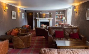 a cozy living room with brown leather couches and chairs , a fireplace , and a fireplace mantle at Fife Arms Hotel