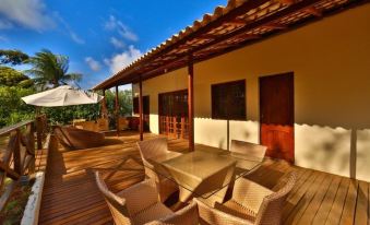 a wooden deck with a dining table and chairs , surrounded by lush greenery and a beautiful blue sky at Pousada Simpatia da Ilha